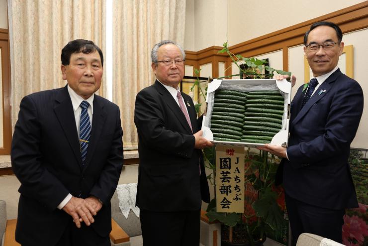 表敬訪問で秩父きゅうりとともに訪問者と記念写真を撮る知事の写真