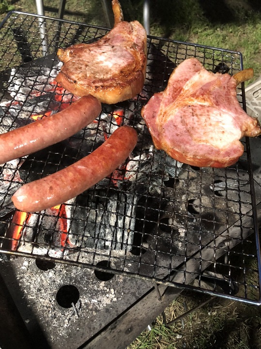 バーベキューで豚肉とソーセージを焼いている写真