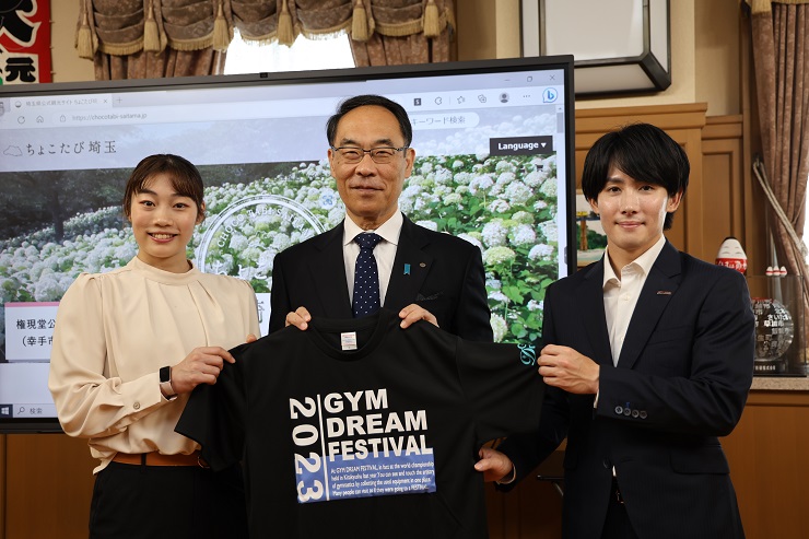 GYM Dream Festival実行委員会会長表敬訪問で大会Tシャツを持ち記念撮影する知事の写真