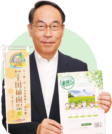 埼玉県知事 大野元裕 写真：全国植樹祭のパンフレットを手に持ち、植樹祭ののぼりとともに撮影