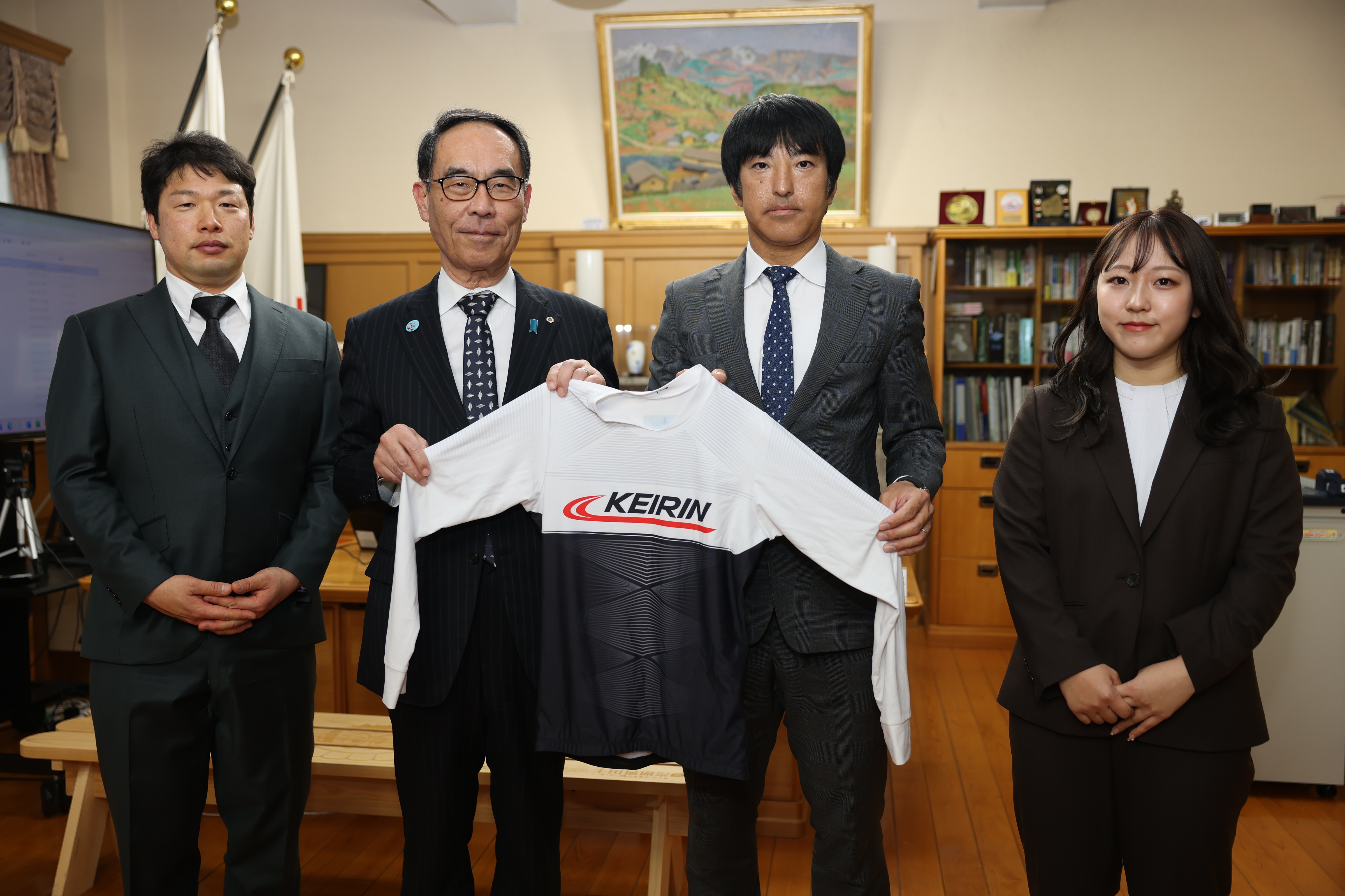 感謝状贈呈者と競輪のウェアを手に取り記念写真を撮る知事の写真